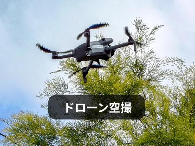 青空の下、樹木の上空を飛行する不動産・建築向け空撮用ドローン