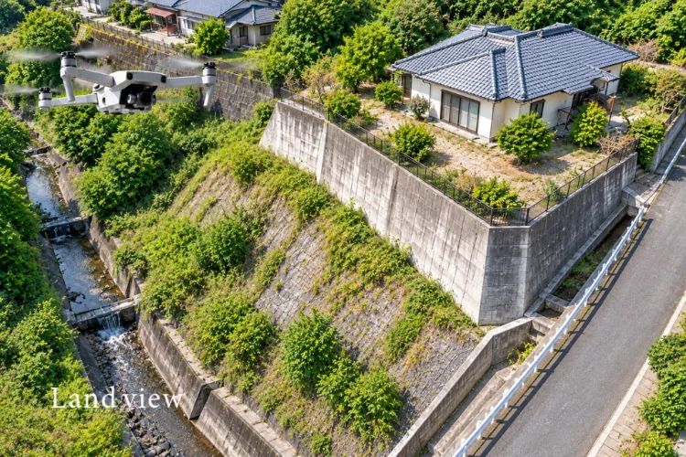 擁壁・法面・排水路をドローンで上空から撮影し、敷地の高低差や排水状況を確認するイメージ